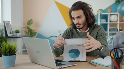 Free Focused young man analyzing financial charts at home office desk. Stock Photo