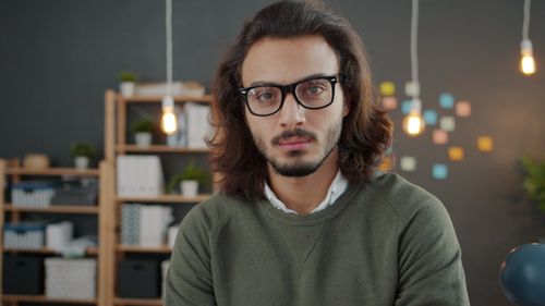 Free Portrait of a young man with glasses and long hair in a stylish office setting. Stock Photo