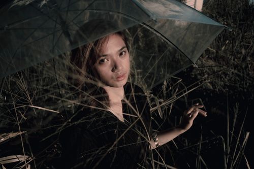 Free Stylish woman posing with transparent umbrella in nature, evoking a mysterious mood. Stock Photo