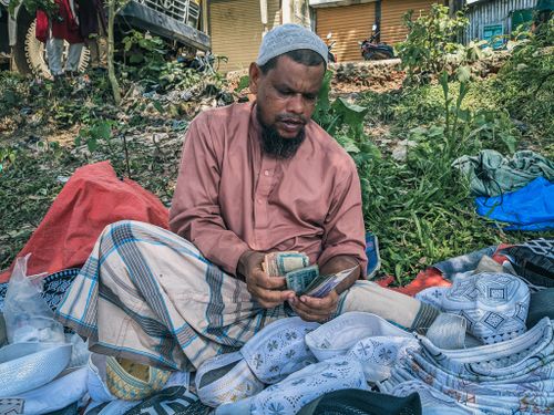 Free A local vendor in Habiganj, Bangladesh counts money surrounded by traditional hats at an outdoor market. Stock Photo