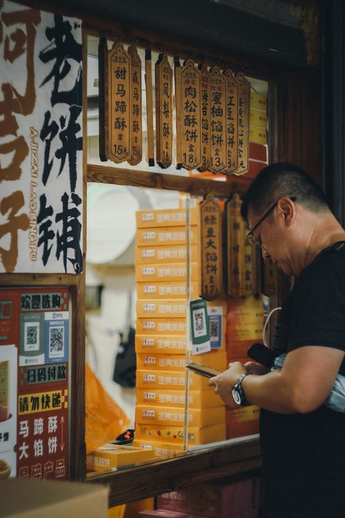 Free Man using a mobile device to pay at a traditional food stall showcasing Chinese signage and menu. Stock Photo