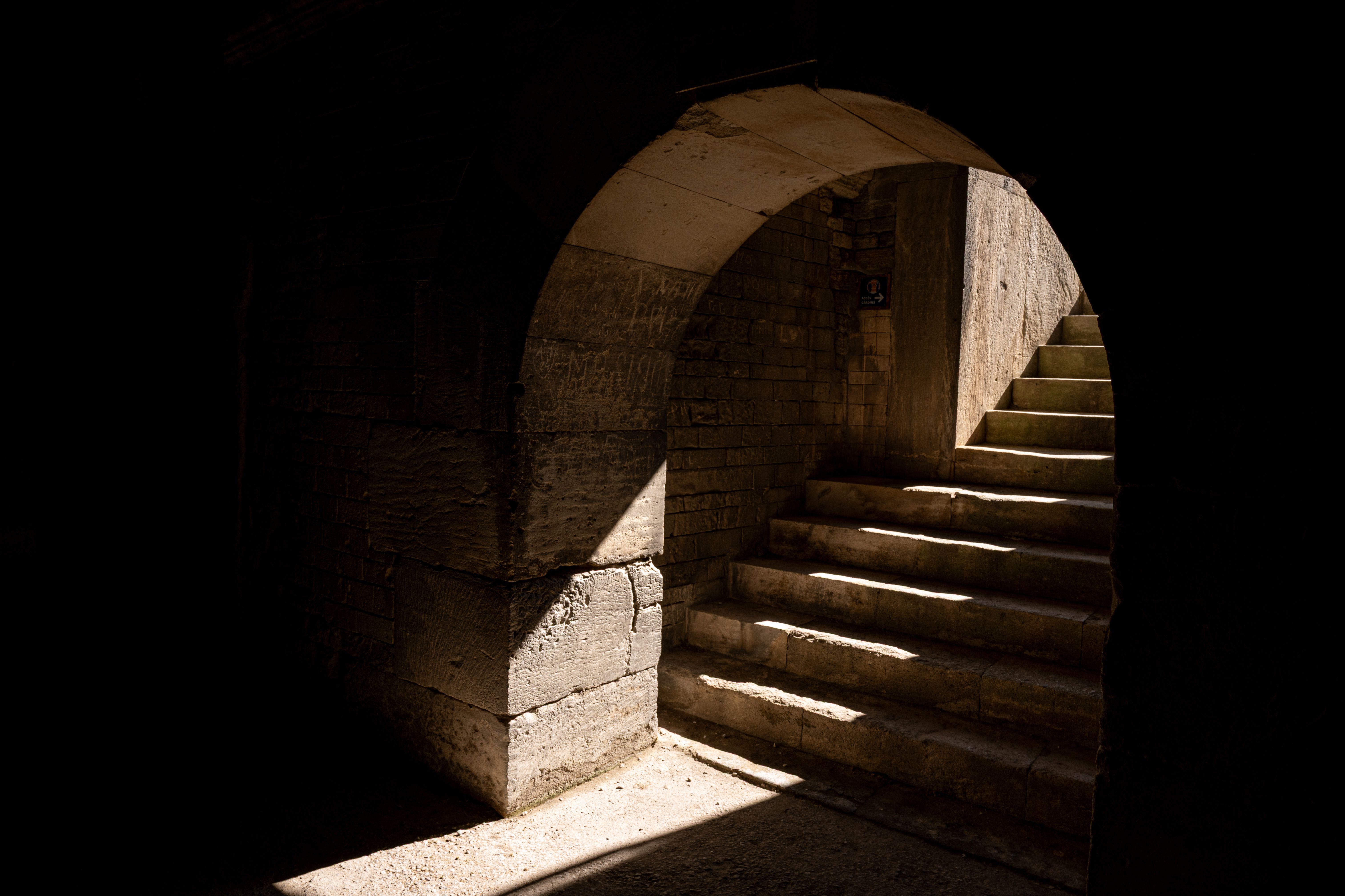 A shadowy stone archway and steps in Arles, capturing historic architecture.