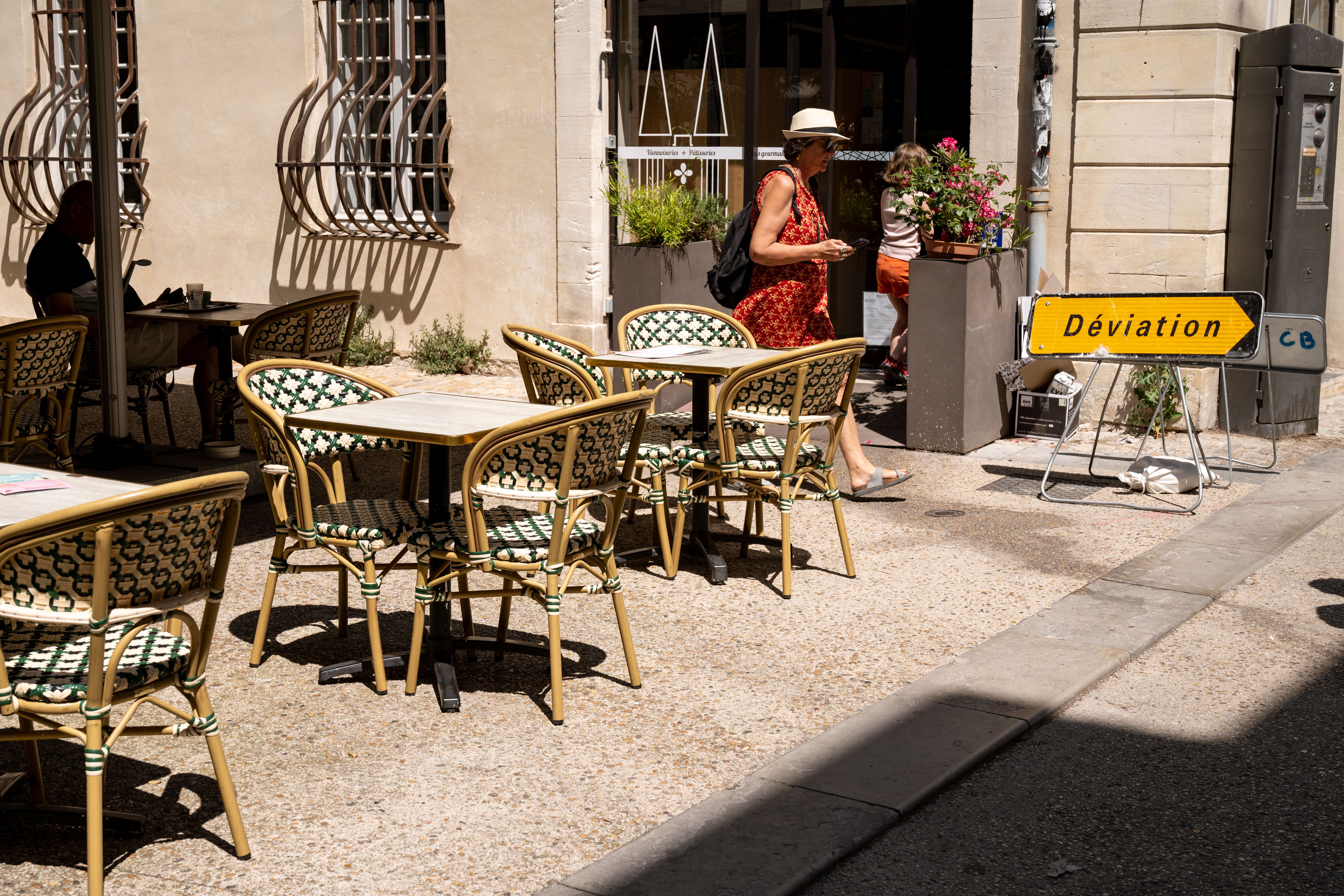 Sunny day at an Avignon café terrace with an outdoor seating arrangement and a woman walking by.
