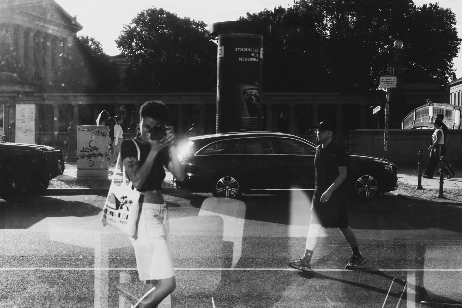 A black and white street reflection with a photographer and pedestrians