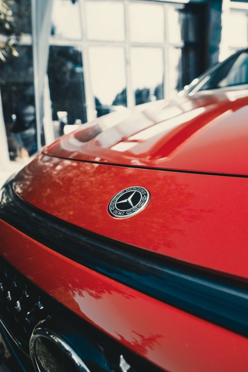 Free Detailed photo of a luxury car emblem on a red vehicle with sunlight reflections outdoors. Stock Photo