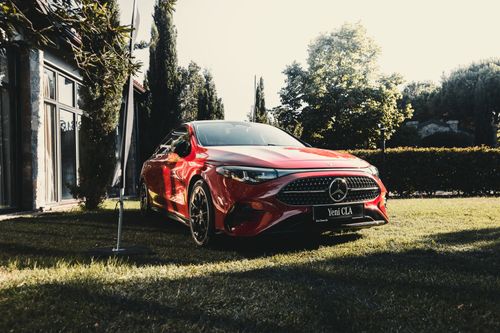 Free Red luxury car on grass with trees and building in a sunny outdoor setting. Stock Photo