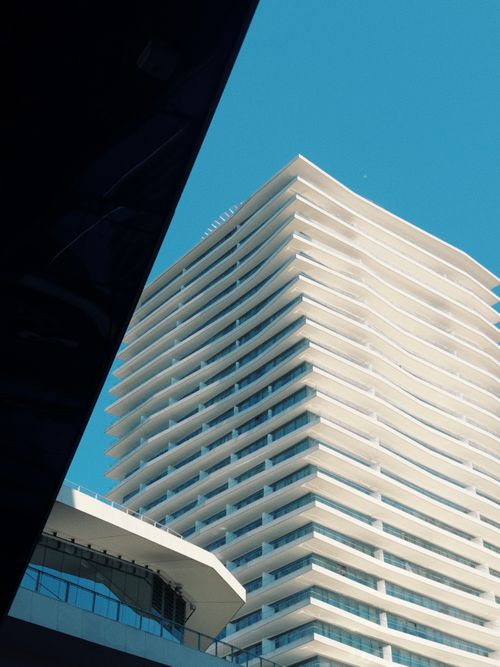 Free A contemporary high-rise building with unique architecture set against a vibrant blue sky. Stock Photo