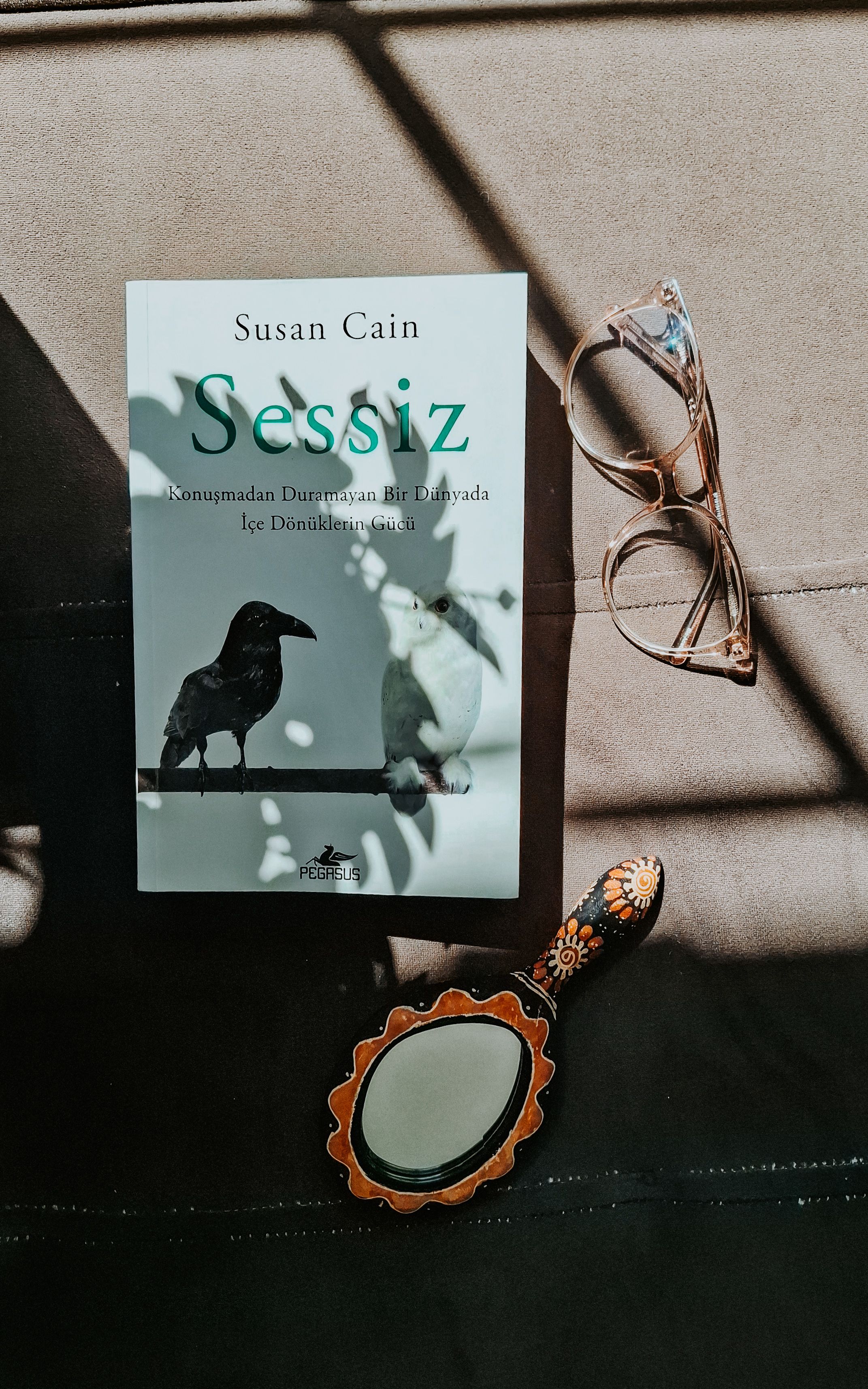 Artistic scene featuring a book, glasses, and a decorative mirror in natural light and shadow.