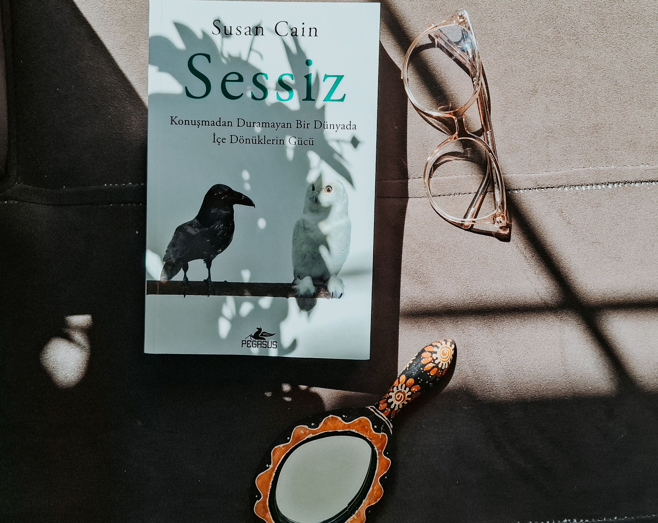 A book, glasses, and mirror on a sunlit surface with shadow patterns.