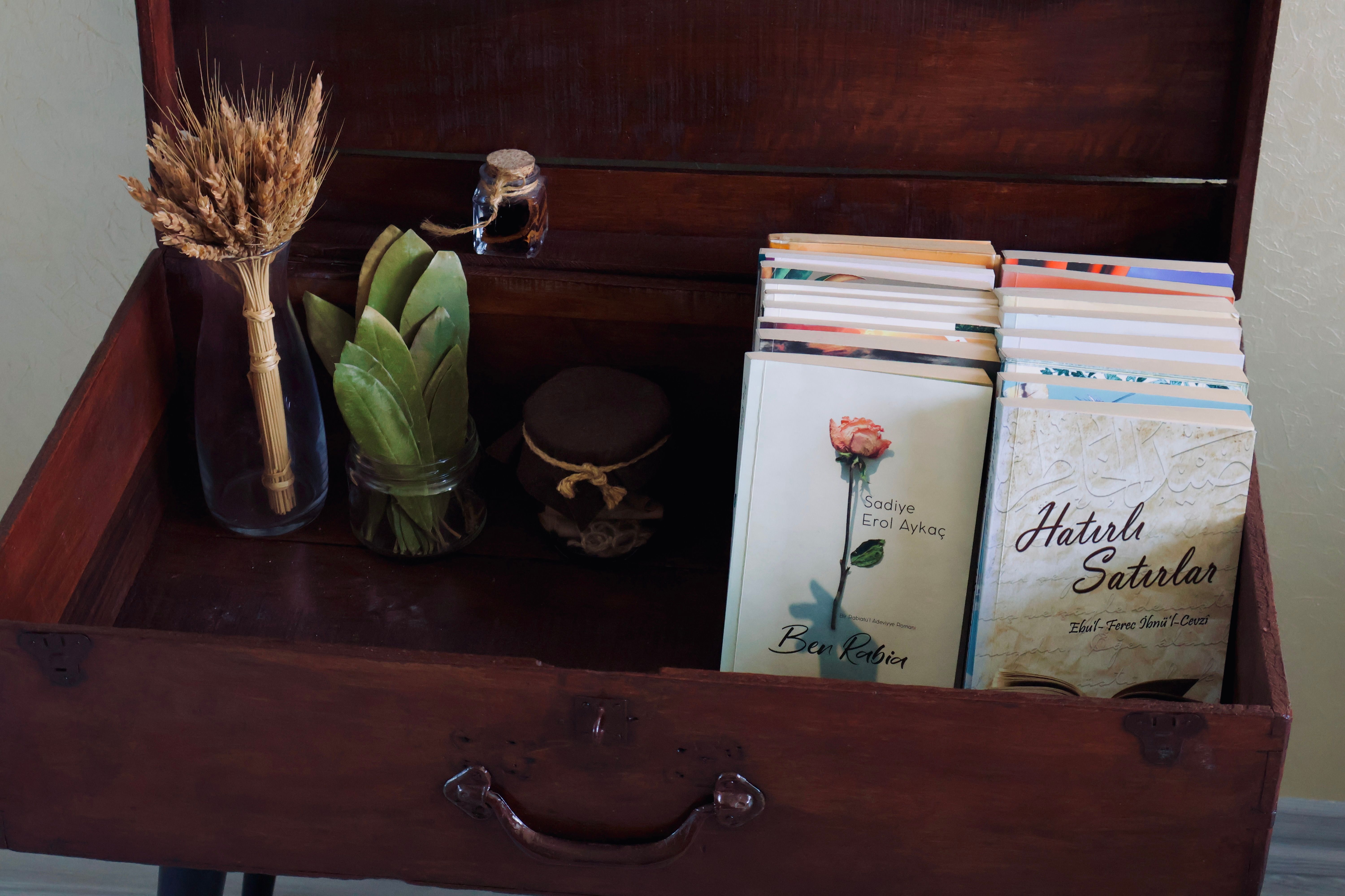 Open wooden box with stacked books, dried wheat, and green leaves.