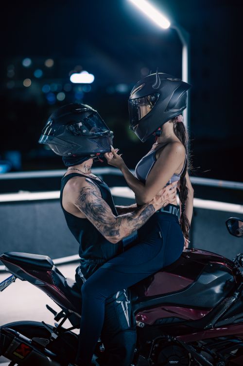 Free A romantic scene of a couple wearing helmets, embracing on a motorcycle under city lights. Stock Photo
