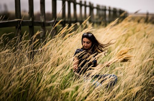 Free A woman sits in a grassy field during sunset, surrounded by tall, golden grasses. Stock Photo