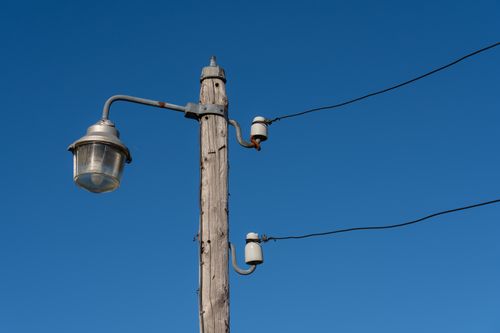 Free A vintage wooden utility pole with wires and street lamp against a clear blue sky. Stock Photo