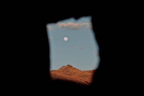 Free Capture of a moonrise over a mountain peak framed by a cave opening, with clear blue sky. Stock Photo