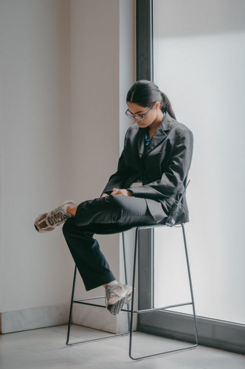 Free A young woman in formal attire sitting near a window, reflecting a modern professional setting. Stock Photo