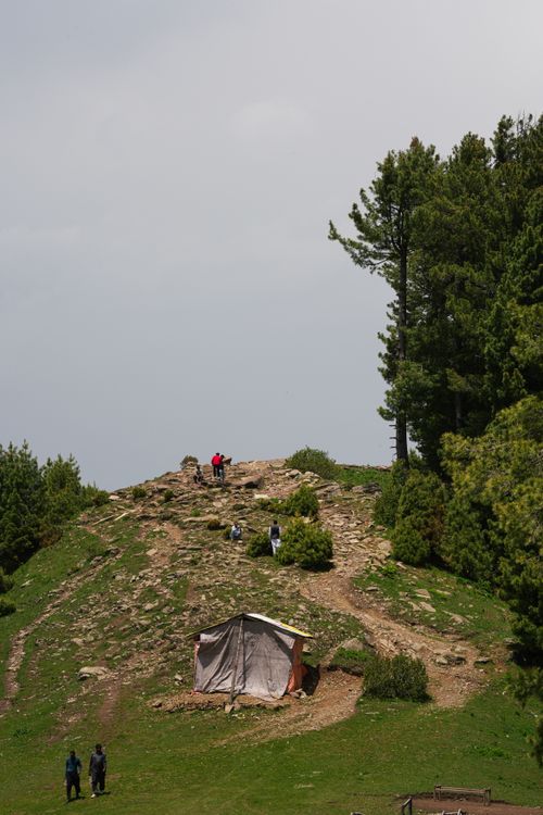 Free A serene hilltop with a tent surrounded by lush greenery and hikers enjoying the view. Stock Photo