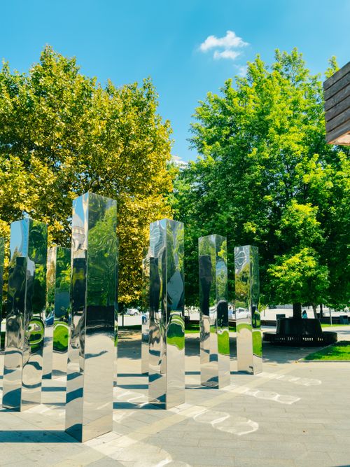 Free Tall shiny metallic sculptures in an outdoor park surrounded by lush green trees under a clear blue sky. Stock Photo