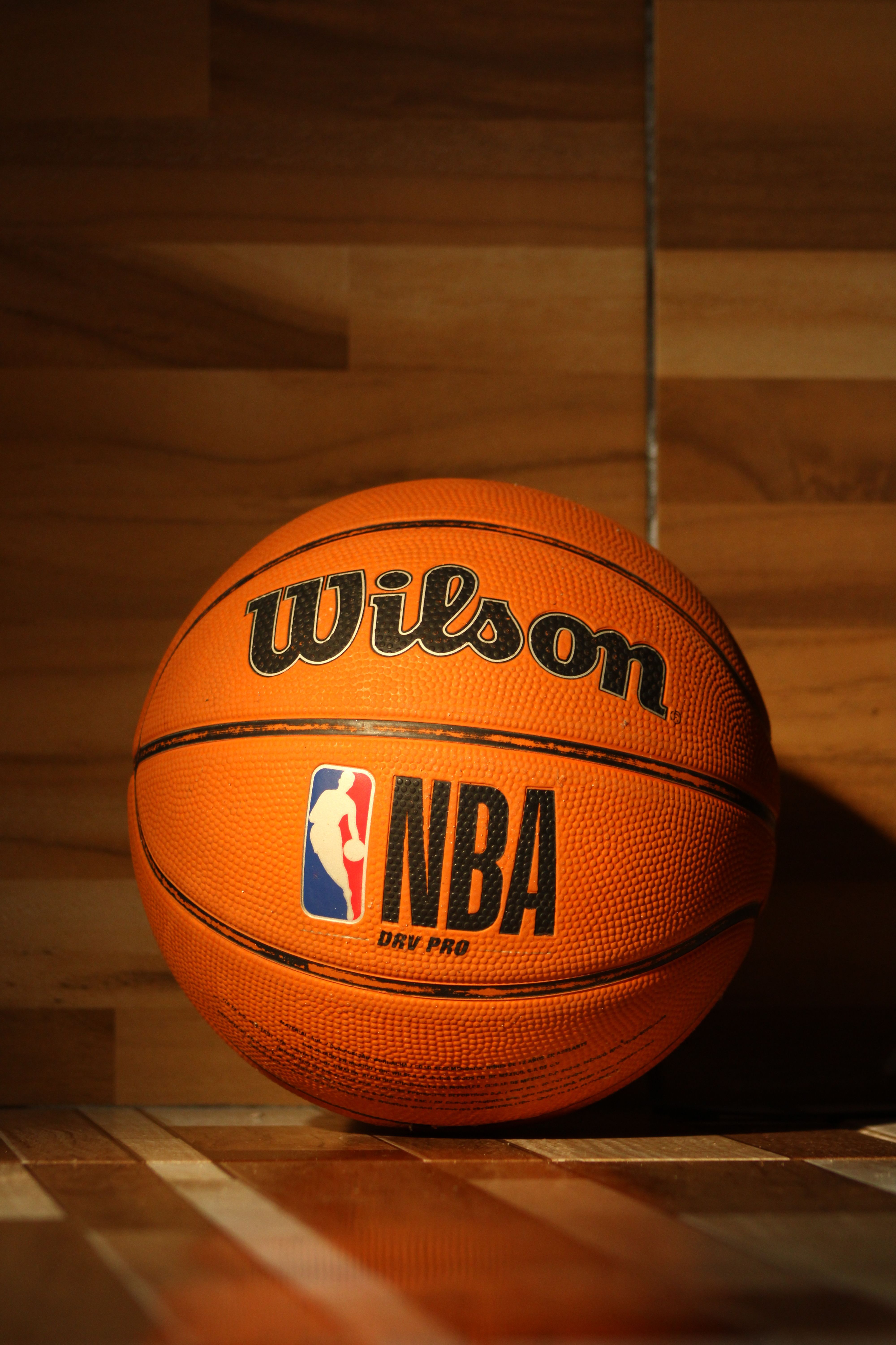 A Wilson NBA basketball sitting on a polished wooden court with dramatic lighting.