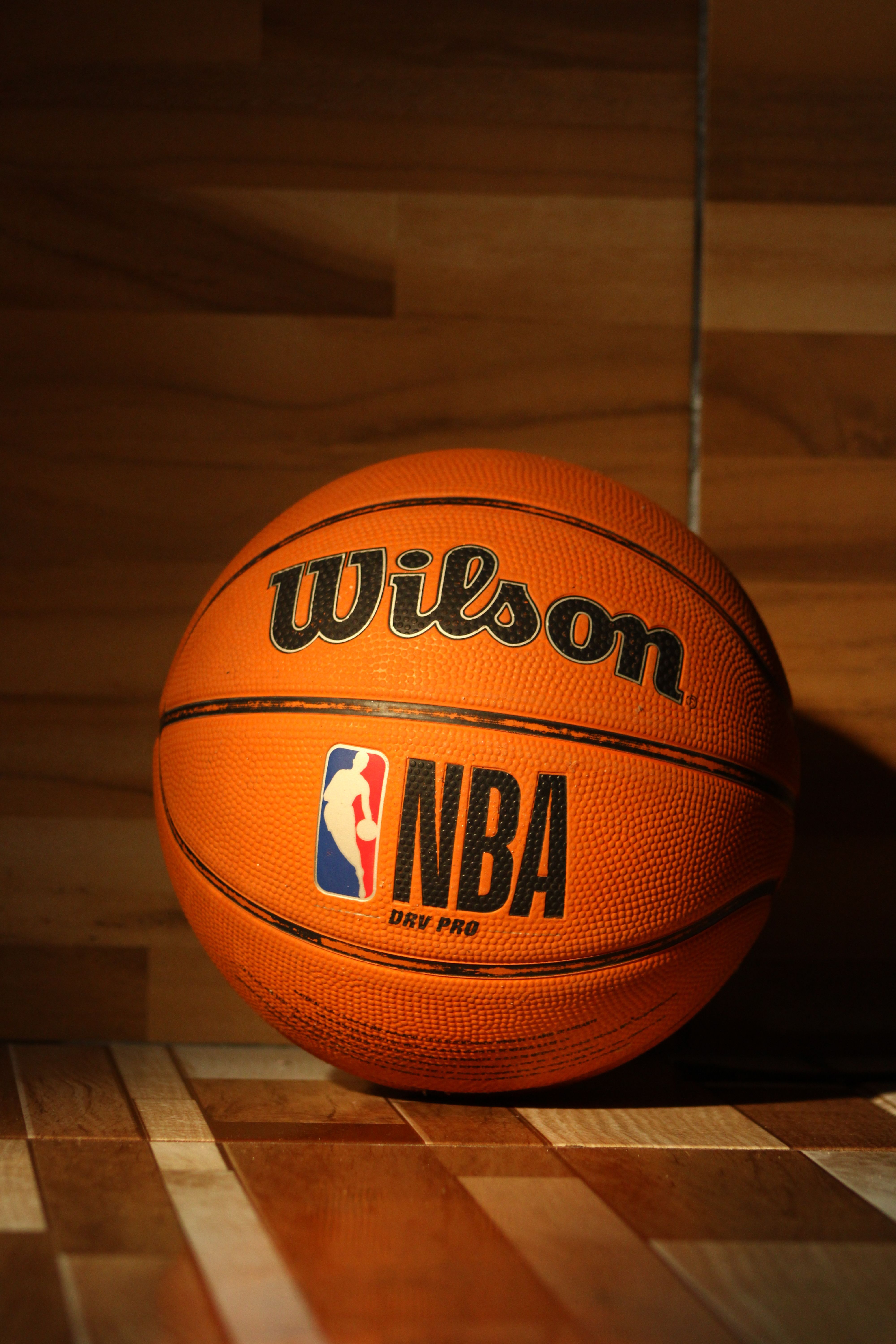 A Wilson basketball with NBA logo resting on a wooden floor, ideal for sports themes.