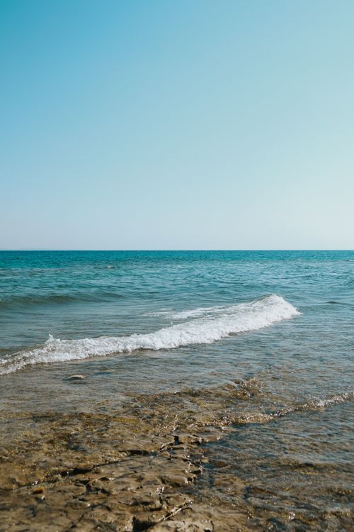 Free Tranquil view of gentle waves lapping at a rocky beachfront under a clear sky. Stock Photo