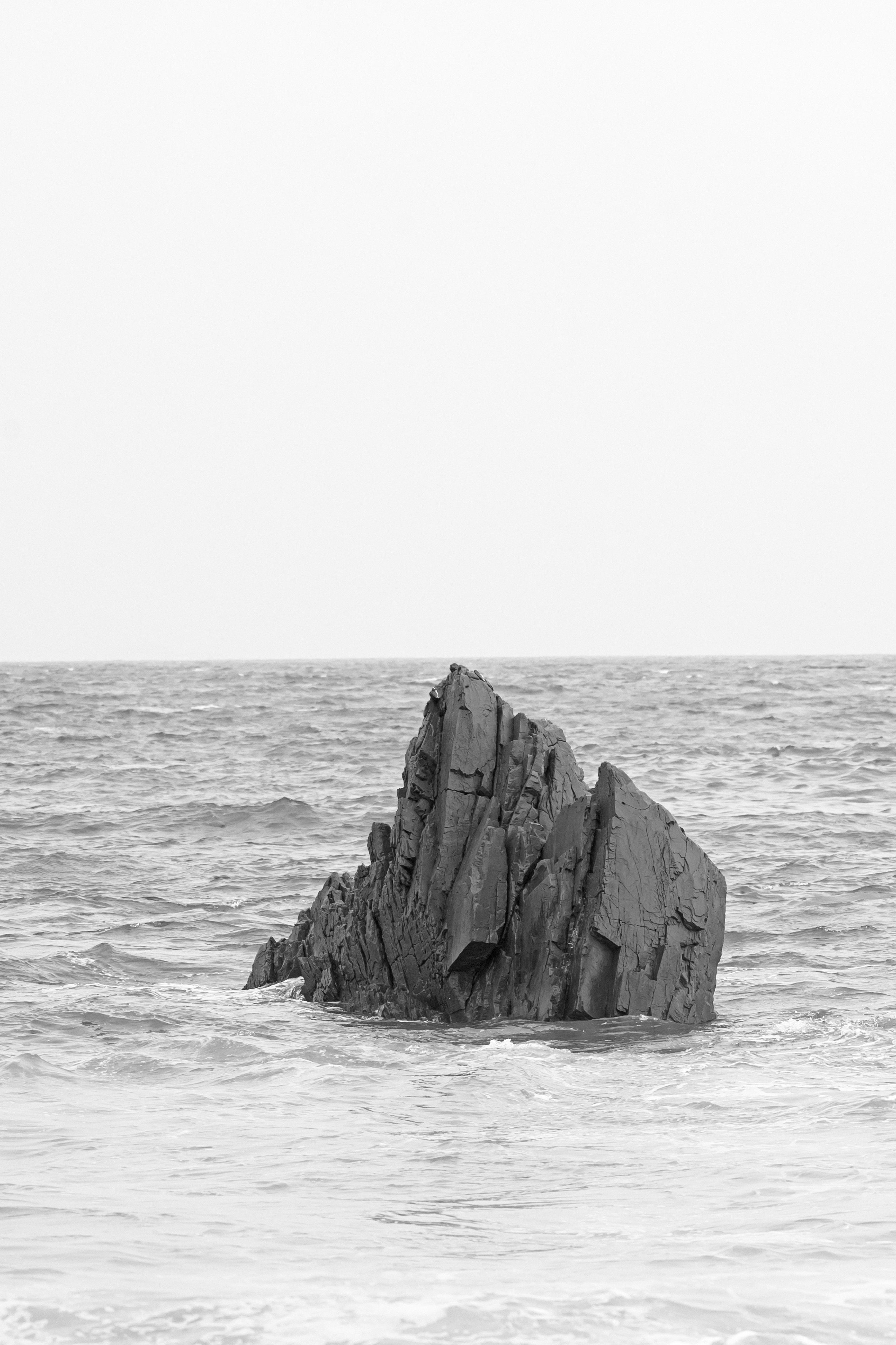A black and white photo of a solitary rock formation standing in the ocean waters.