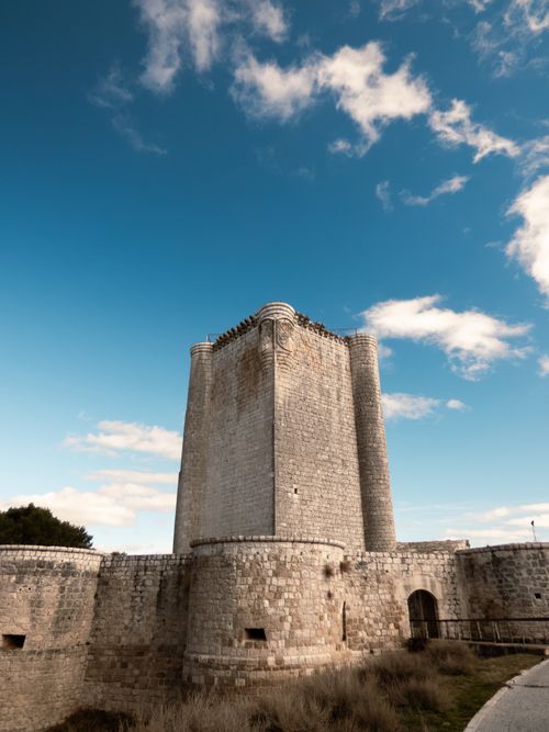 Free A towering medieval stone fortress under a bright blue sky, showcasing historic architecture. Stock Photo