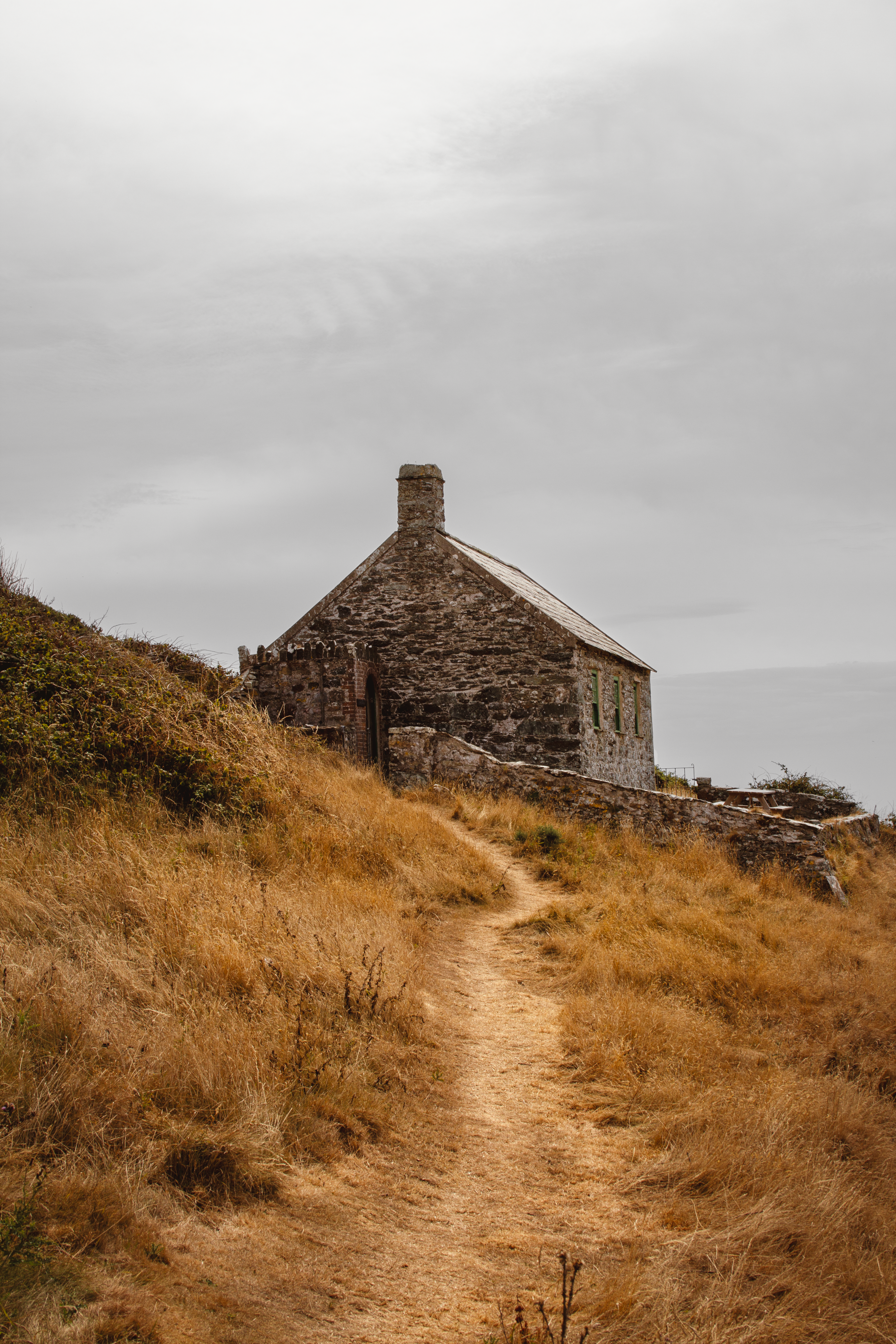 A rugged stone house amid dry grass on a hill in Wales, displaying rustic charm.