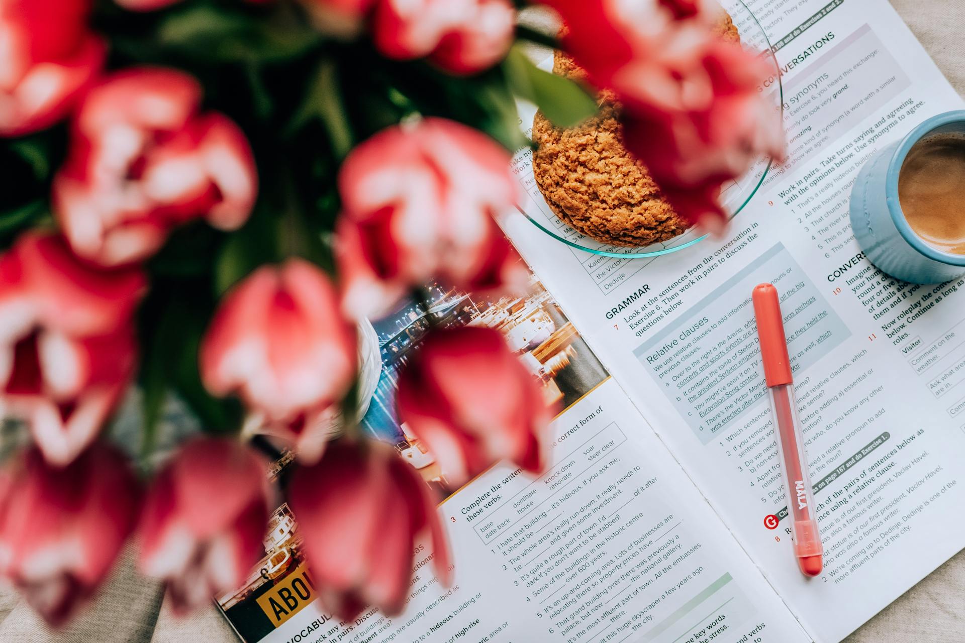 From above bouquet of tulips placed near cookies and mug of coffee on English textbook on table