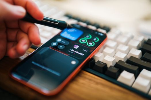 Closeup of a hand using a stylus on a smartphone, showcasing a modern digital workspace.