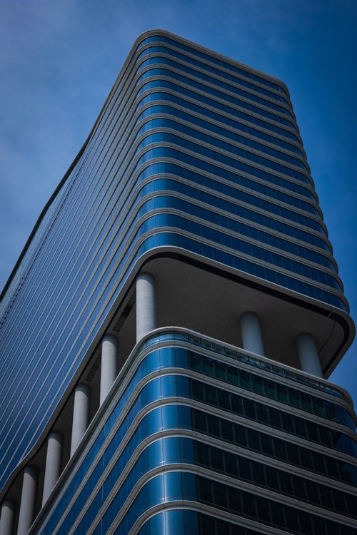 Free A sleek, modern skyscraper with reflective windows against a clear blue sky. Stock Photo