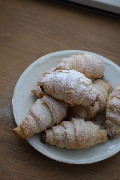 Free A plate of homemade croissants dusted with powdered sugar, presented on a wooden table. Stock Photo