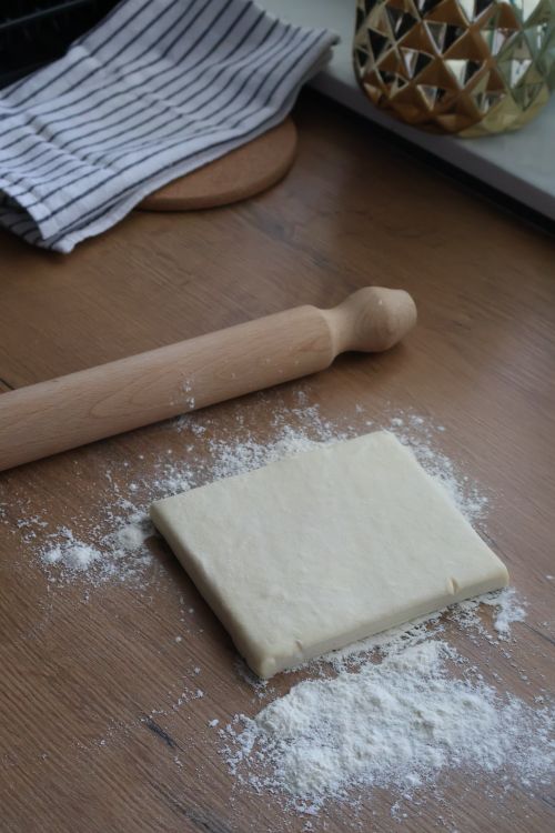 Free Square pastry dough on a floured wooden surface with rolling pin and cloth nearby. Stock Photo