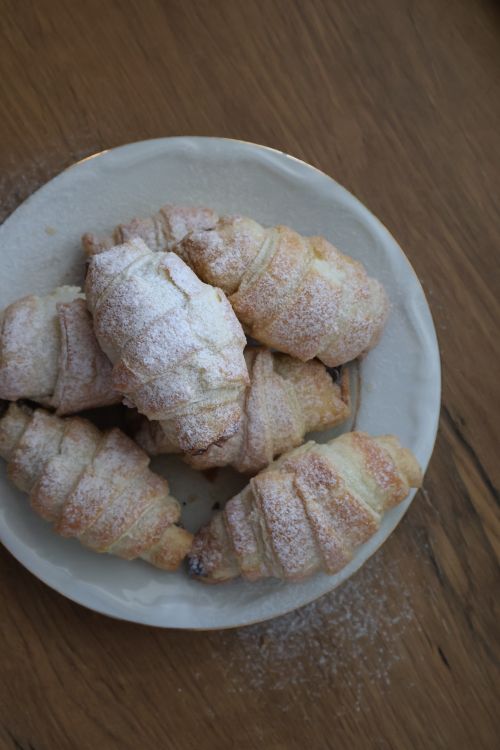 Free A plate of golden-brown, flaky croissants dusted with powdered sugar. Stock Photo