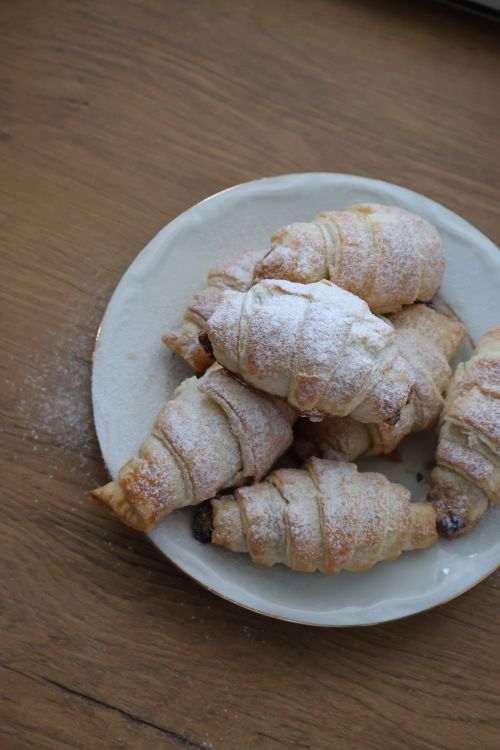 Free Freshly baked croissants with powdered sugar on a white plate on a wooden table. Stock Photo