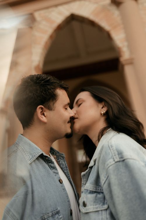Free A couple wearing denim jackets share a tender kiss in a romantic setting with arches. Stock Photo