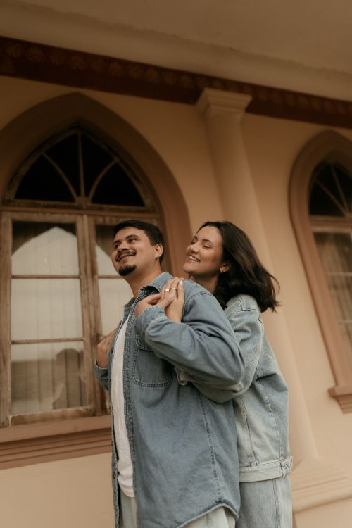 Free A joyful couple in denim standing outside a historical building with arched windows. Stock Photo