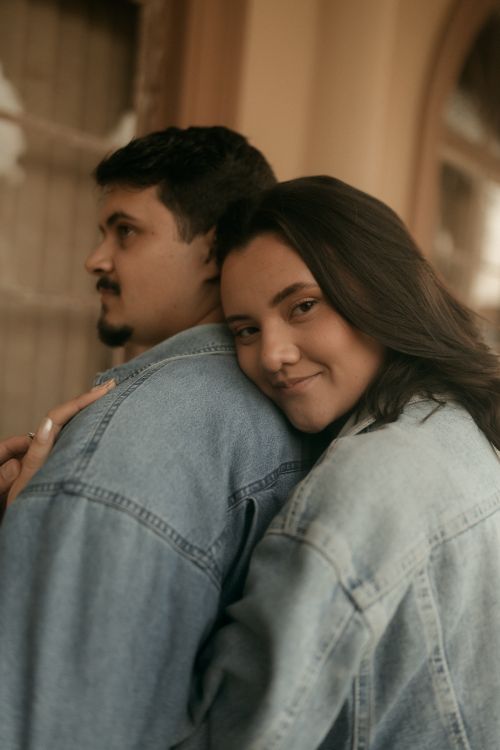 Free Young couple embracing, both wearing denim jackets, conveying warmth and affection in an indoor setting. Stock Photo