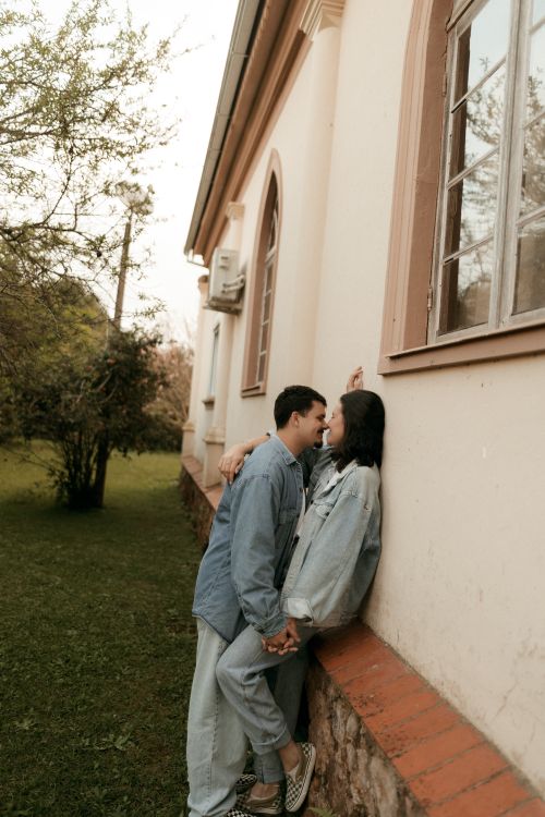 Free A young couple in denim outfits embraces affectionately by an outdoor wall. Stock Photo