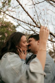 A loving couple shares a tender moment beneath blossoming branches in a serene outdoor setting. - Fotografer Sidoarjo