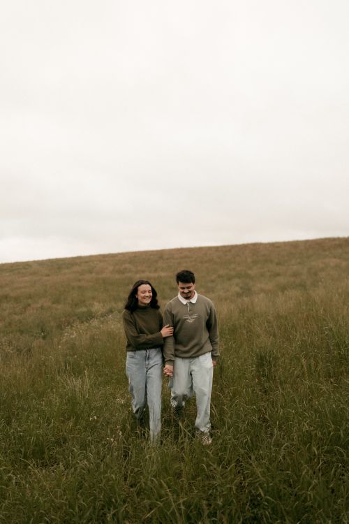 Free A young couple enjoys a stroll through a serene grassy meadow on a cloudy day. Stock Photo