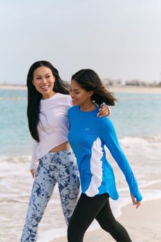 Two women in activewear jogging happily on a beach in the UAE.