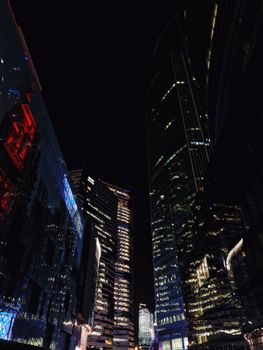 City skyline at night with illuminated skyscrapers and vibrant reflections.