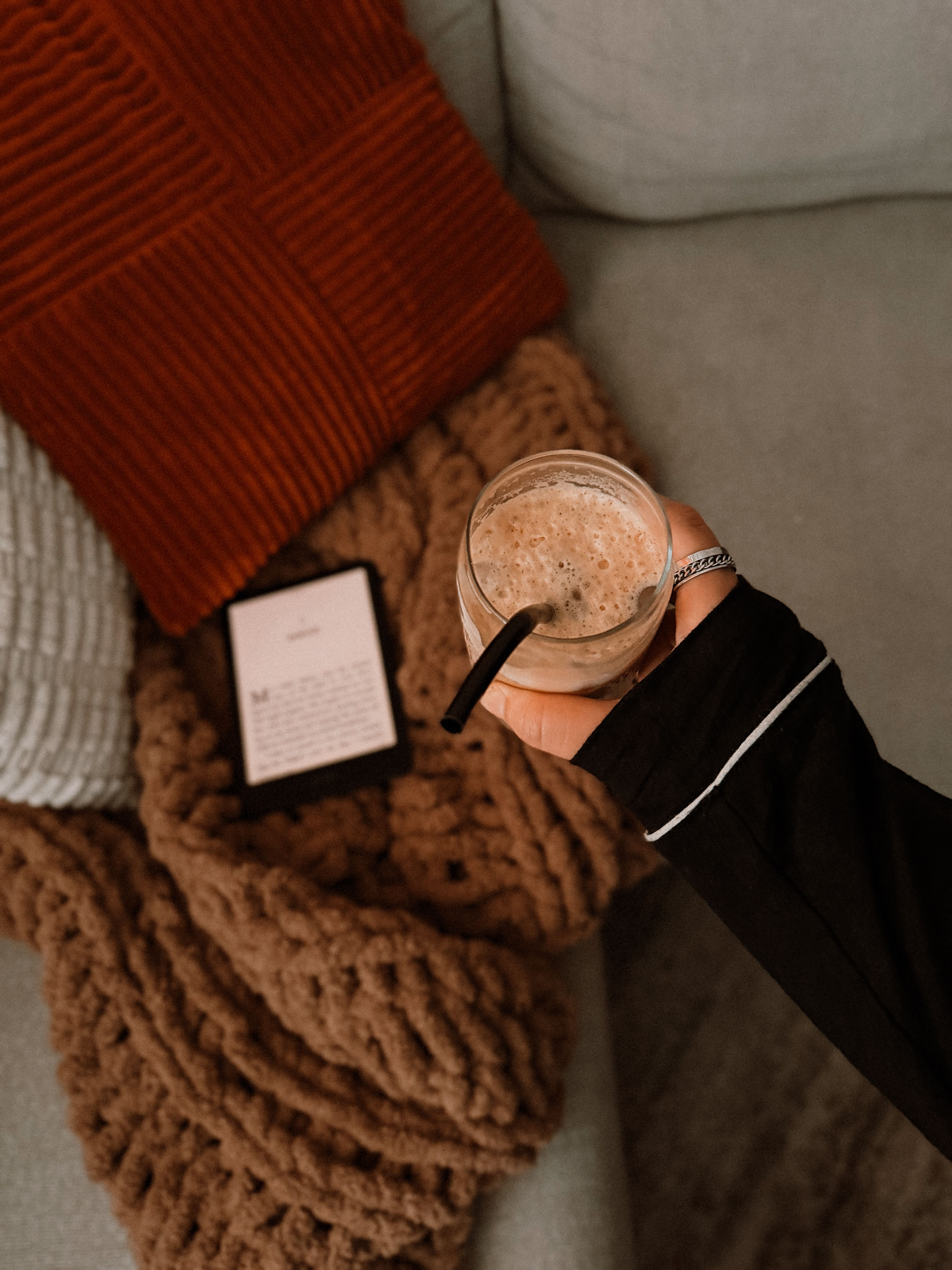 A cozy setting with a warm knit blanket, drink, and e-reader on a couch.