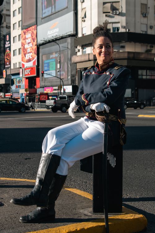 Free Woman in historical military uniform seated outdoors in a city setting, capturing a blend of past and present. Stock Photo