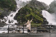 一名妇女在郁郁葱葱的绿植间，欣赏着瀑布的壮丽景色