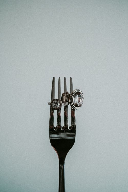 Free Three elegant rings creatively displayed on a shiny silver fork, emphasizing artful presentation. Stock Photo