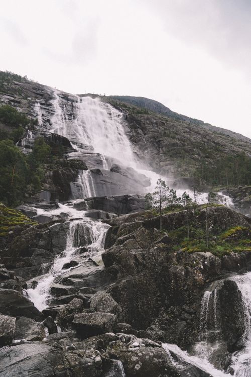 Free A scenic waterfall cascading down rugged rocks in a misty mountain landscape. Stock Photo