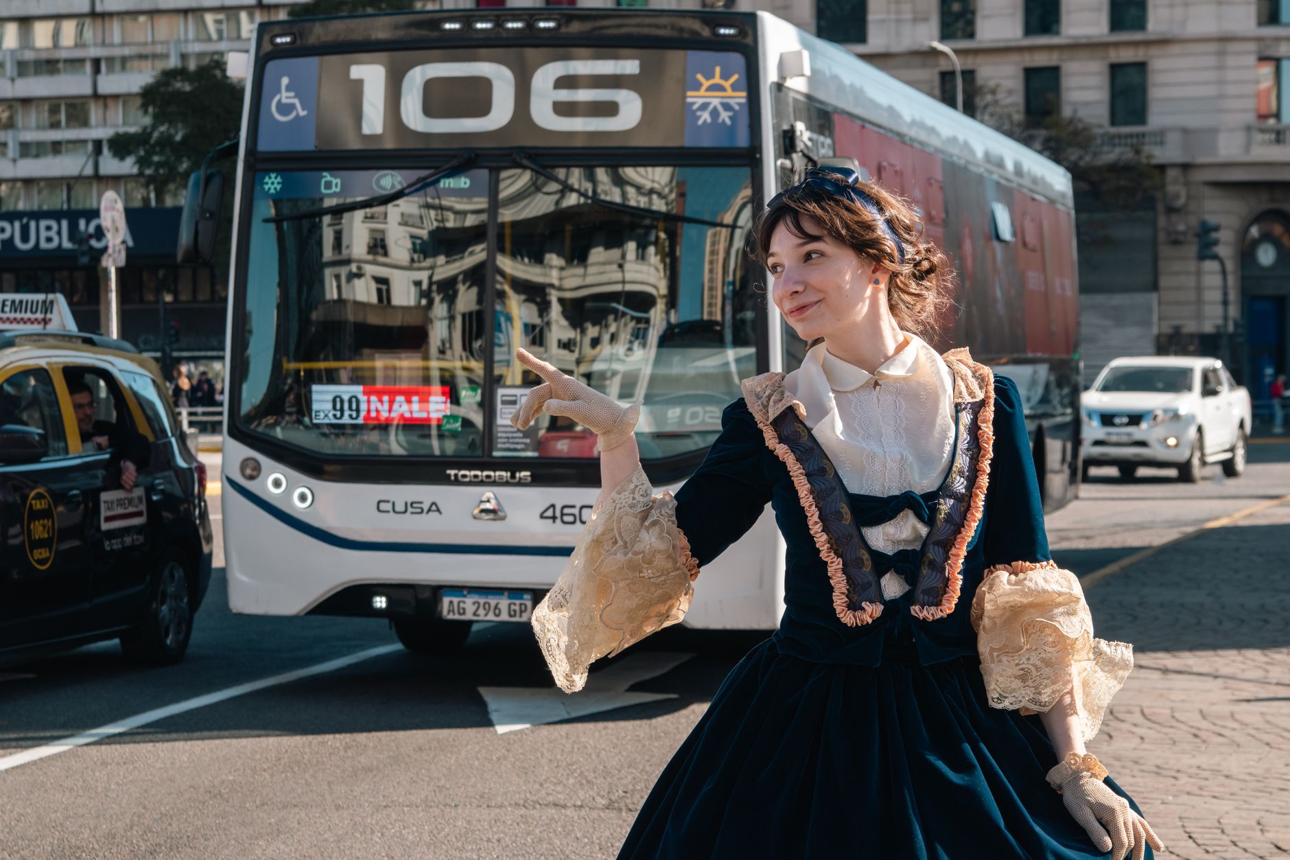 A woman in a vintage dress stands in front of a city bus on a busy street.