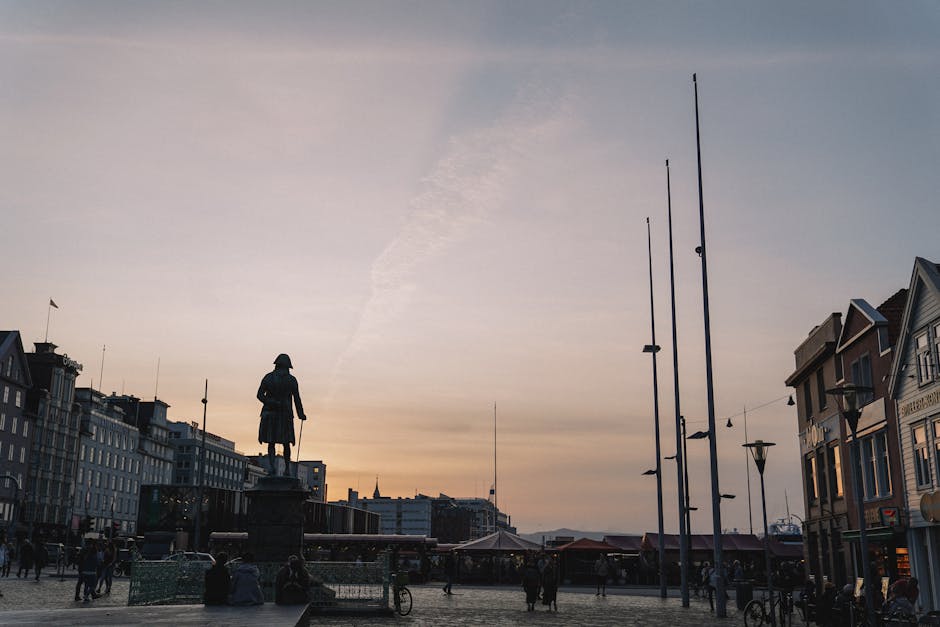 Silhouetted statue and city buildings against a sunset sky.