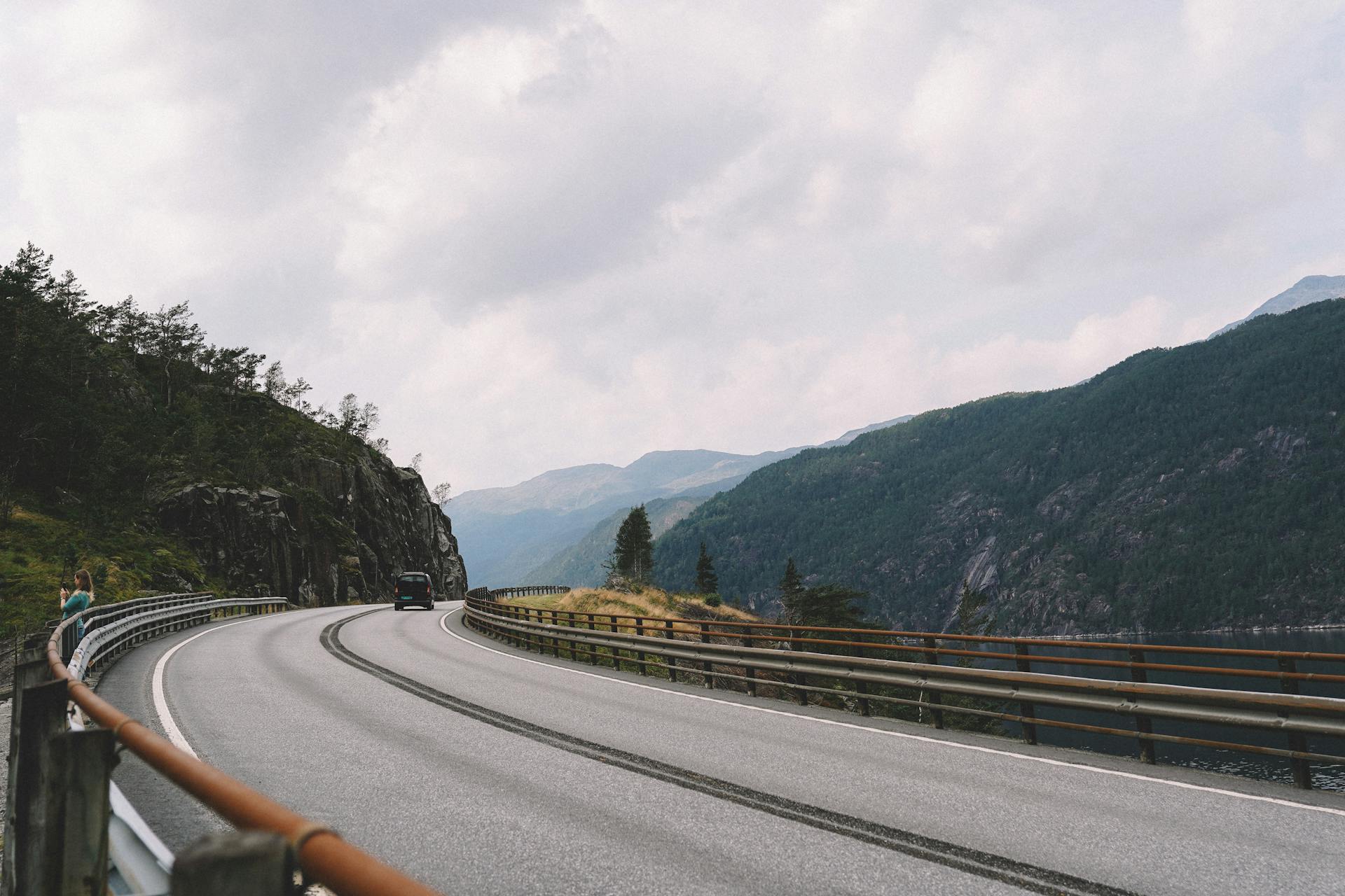 A picturesque road curves along a mountain cliffside under a cloudy sky, ideal for travel and adventure themes.